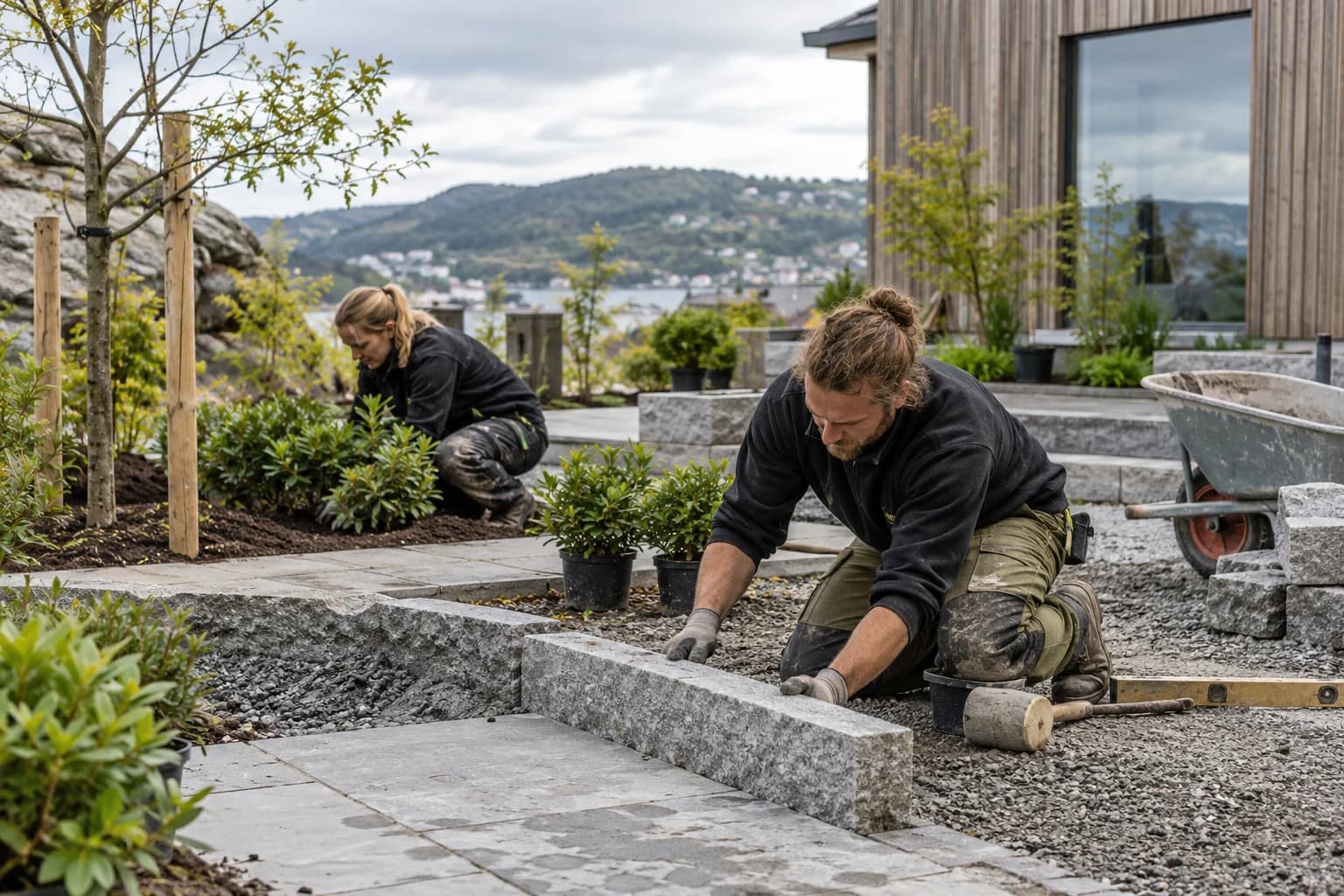To anleggsgartnere legger granittstein og planter busker ved en gangsti